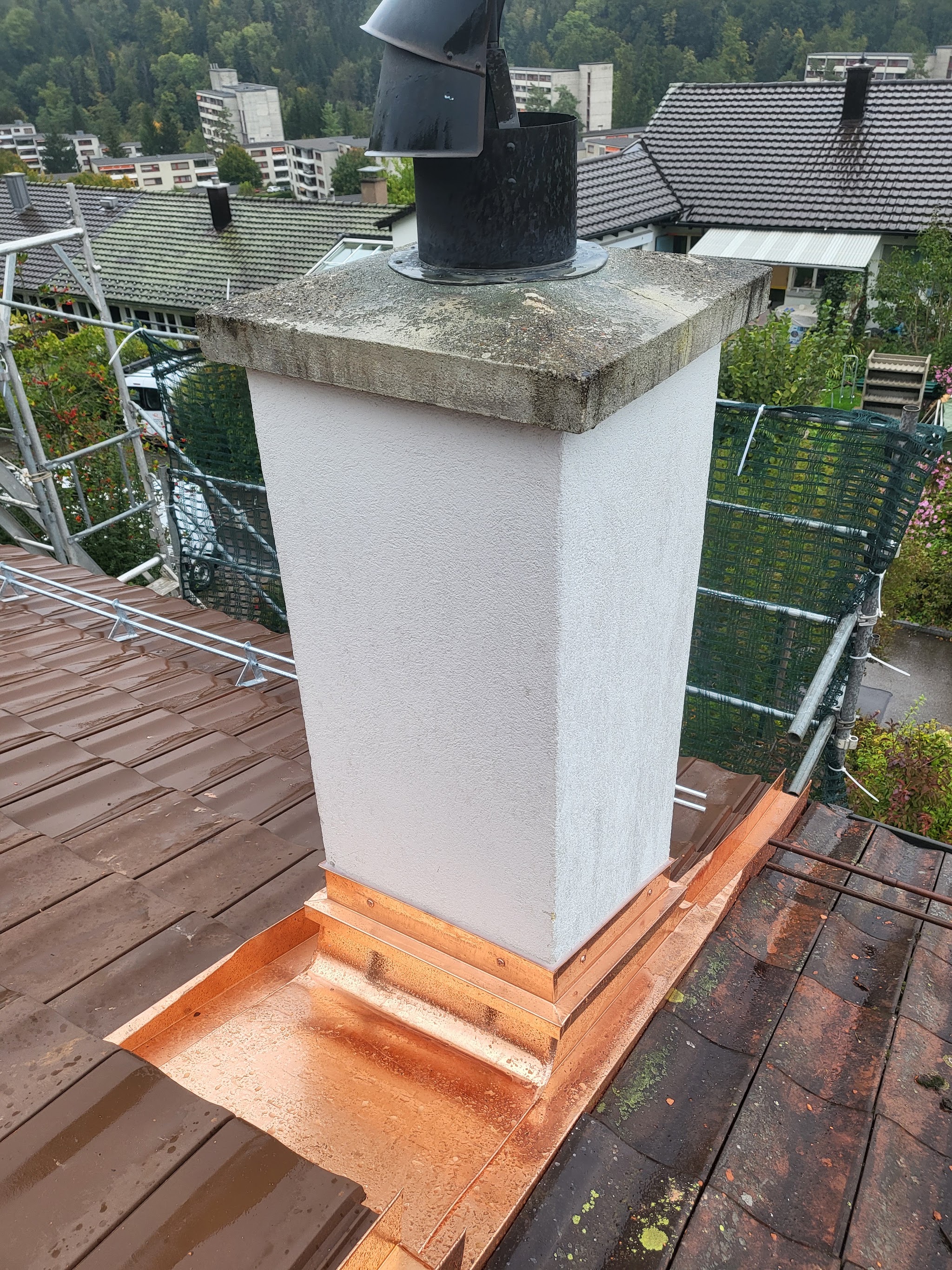 Weisser Kamin mit Kupferkragen auf einem Ziegeldach, Gerüstnetz im Hintergrund